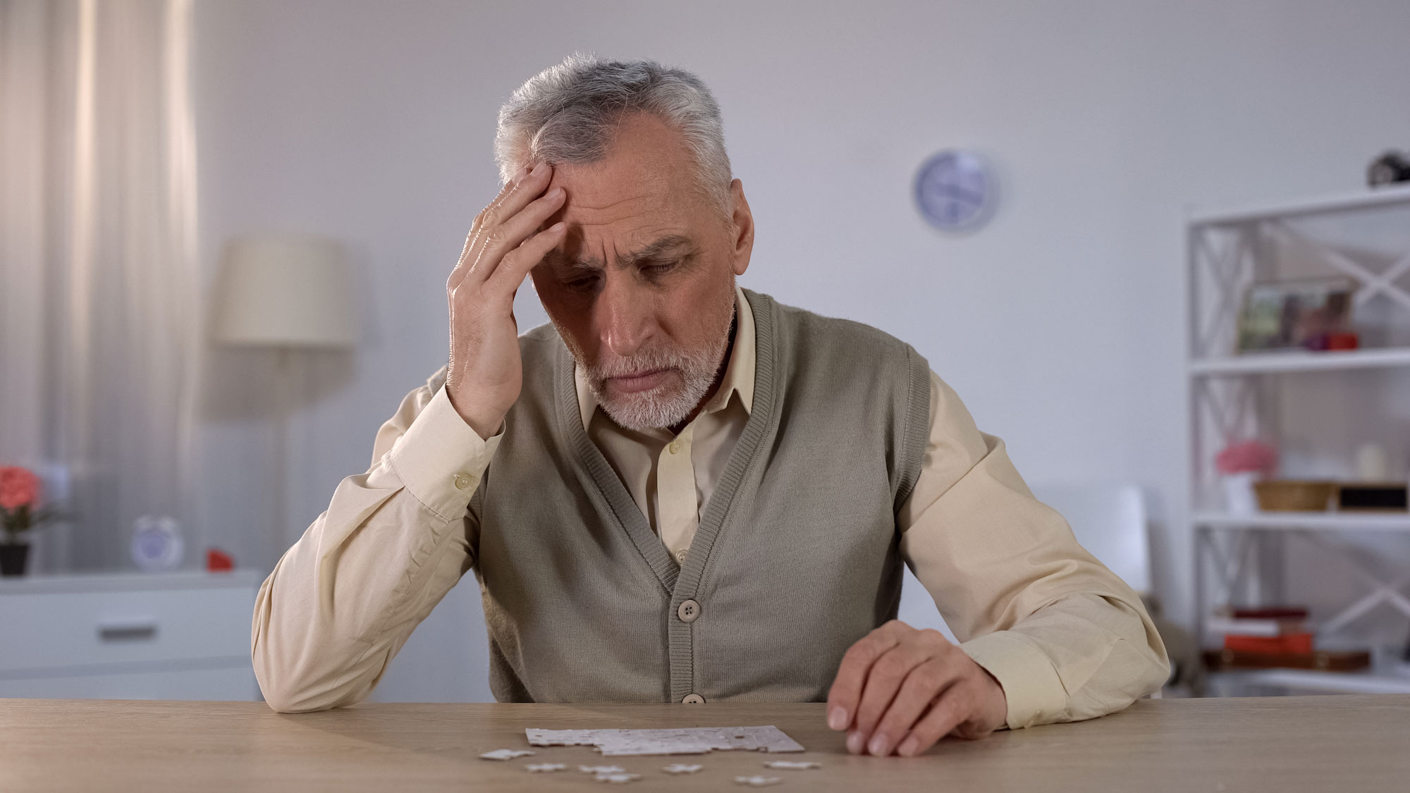 a senior man places hand on head while doing puzzle