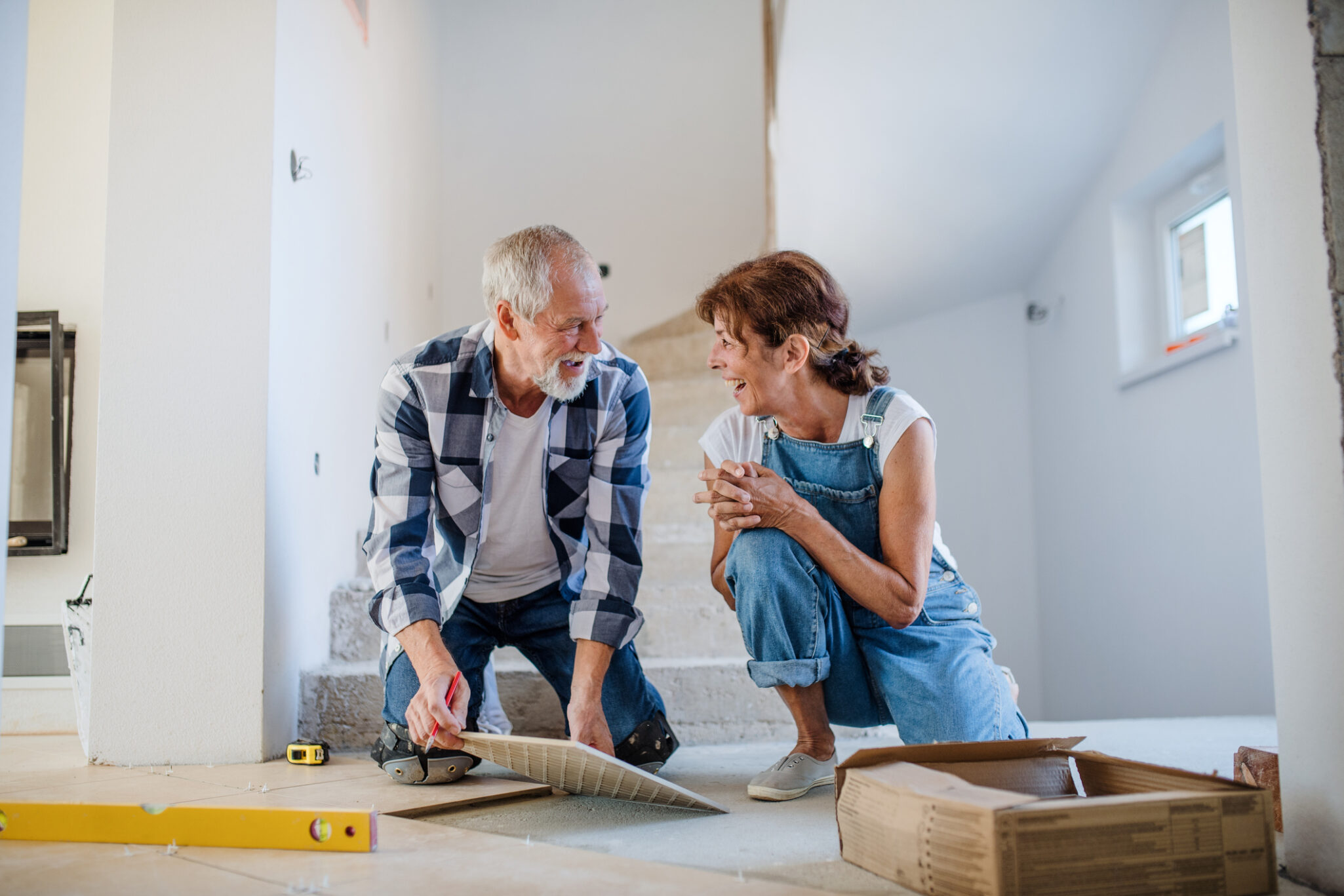 A man and a woman are laying down large tile squares in their home hallway